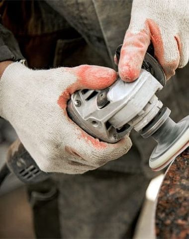 Hände mit Handschuhen beim Schleifen eines Grabsteins mit einer Maschine